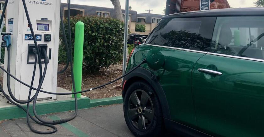A green Mini is backed in to a parking space, and connected to a white-colored charging station.
